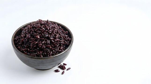 Cooked black rice piled in a dark ceramic bowl with a few grains scattered on a white background.