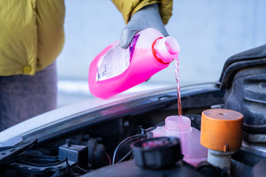 Driver topping up coolant under open hood, Closeup of coolant being poured into engine reservoir, Vehicle servicing moment showing fluid refilling and roadside readiness