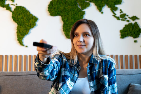 woman has switched channels with the remote control and is looking at the TV screen with interest. television, watching movies and TV series