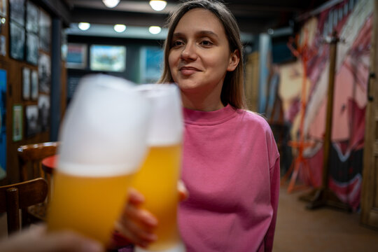 Happy woman laughing and holding a beer glass while sitting with friends in a pub. Toast, social gathering, and joyful nightlife.