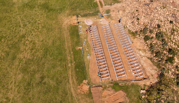 Aerial view of a ground-mounted solar energy installation under construction with workers assembling steel mounting structures on a rural site in Vaalwater, Limpopo, South Africa.