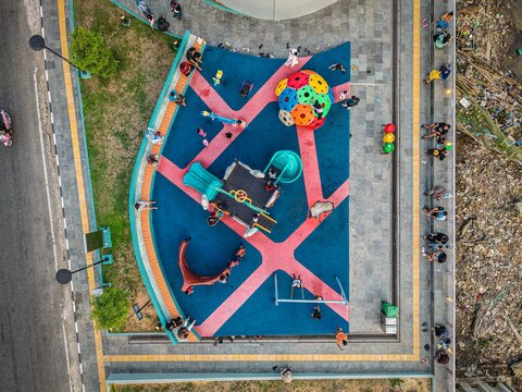 Aerial view of Teras Samarinda 2 playground with colorful play equipment, rubber flooring, and people sitting on the surrounding benches in Samarinda, East Kalimantan, Indonesia.