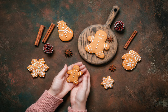 Female hands holding gingerbread man on dark grunge table, Christmas various gingerbread cookies, top view, flat lay.