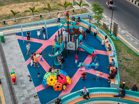 Aerial view of Teras Samarinda 2 playground with children playing on slides and swings, surrounded by parents sitting on curved benches in Samarinda, East Kalimantan, Indonesia.