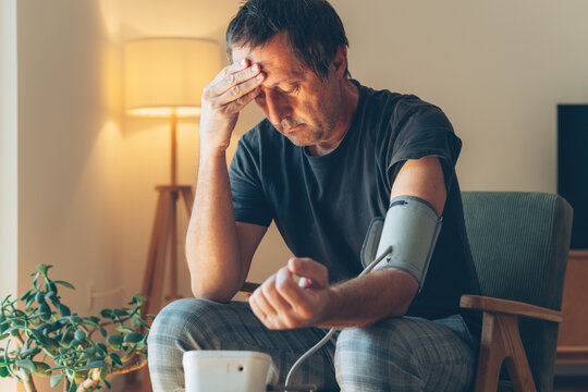 Mature man measuring his own blood pressure with a digital monitor at home, healthcare and wellness concept, comfortable indoor setting with soft lighting.
