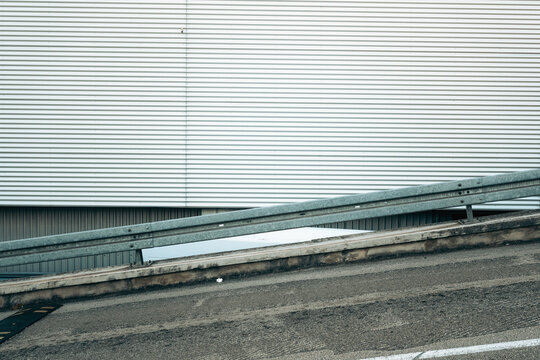 Metal guardrail along an inclined asphalt road in front of a white corrugated industrial building facade.