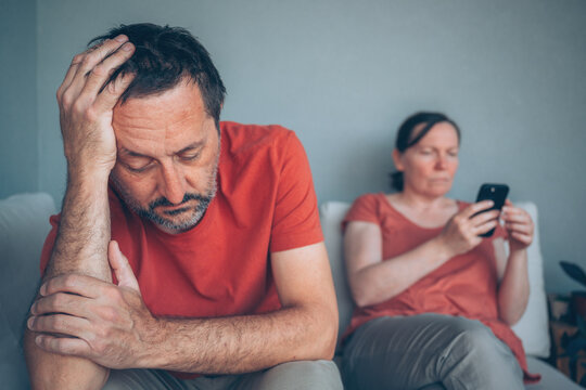 Distant couple sitting on sofa during relationship strain while woman focuses on phone