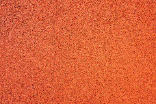 Granular red rubber texture of an athletic running track. Concept of sports performance, athletic training, outdoor fitness facilities, and synthetic flooring materials.
