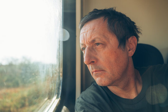Close-up portrait of a middle-aged man staring out the window while riding inside a passenger train.