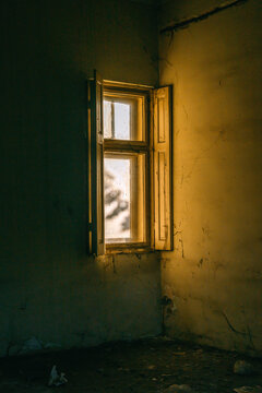 Weathered window and peeling wall inside a derelict room, golden light streaming in, concept of abandonment, decay and forgotten places