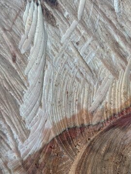 Close up of a pale weathered wooden surface with curved grooves, intersecting tool marks and natural beige and brown tones forming an abstract rustic texture.