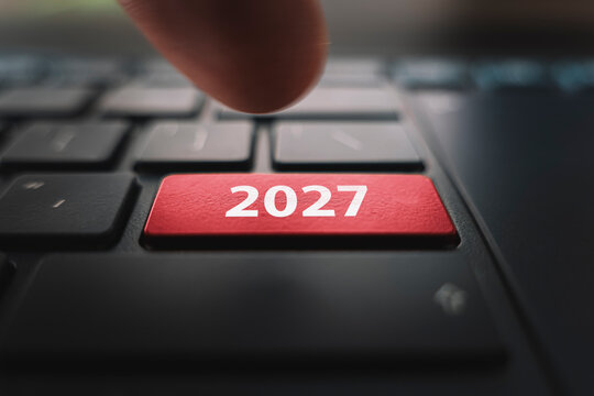 Keyboard with text 2027 year and finger pushing the enter button. Red Color button on the black keyboard of modern ultrabook. caption on the button