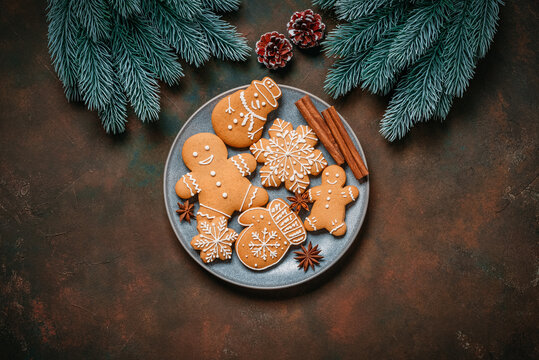 Christmas gingerbread cookies on a plate and decorative spruce branches on a dark rustic background, top view, flat lay, copy space