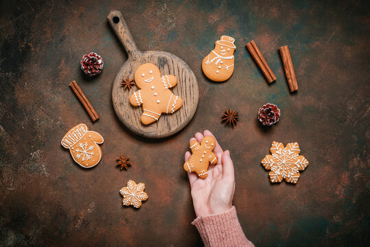 A woman's hand places a gingerbread man on a dark rustic background, top view