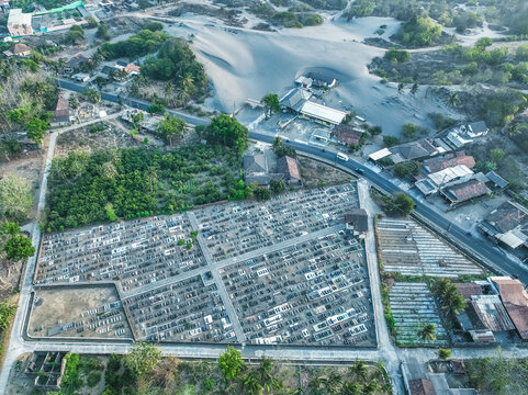 Aerial view of Kabanaran Bridge and the adjacent cemetery with rows of graves, surrounded by sand dunes, trees, and rural roads, Kecamatan Srandakan, Daerah Istimewa Yogya, Indonesia.