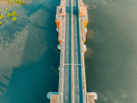Aerial view of Kabanaran Bridge with its distinctive orange supports spanning over the river in Kecamatan Srandakan, Daerah Istimewa Yogya, Indonesia.