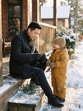 Man and Toddler Untangling Christmas Lights in Snow