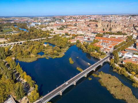 Aerial view of the historic city with the Tormes River, Roman bridge, and cathedral, surrounded by autumn trees under a clear blue sky, Salamanca, Castile and Leon, Spain.