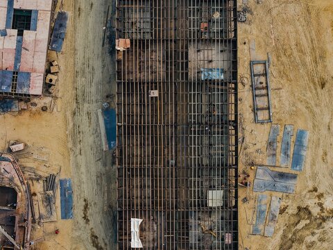 Aerial view of the PT. Menumbar Kaltim shipyard showing the metal framework of a large vessel under construction, surrounded by sandy ground in Samarinda, Kalimantan Timur, Indonesia.