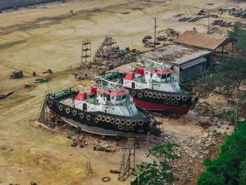 Aerial view of PT. Menumbar Kaltim shipyard showing two tugboats undergoing maintenance with workers, scaffolding, and industrial equipment in Samarinda, Kalimantan Timur, Indonesia.