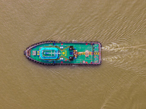 Aerial view of a green tugboat navigating the Mahakam River, leaving a wake in the murky water in Samarinda, East Kalimantan, Indonesia.