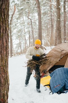 Man collecting firewood for winter camping in snowy forest