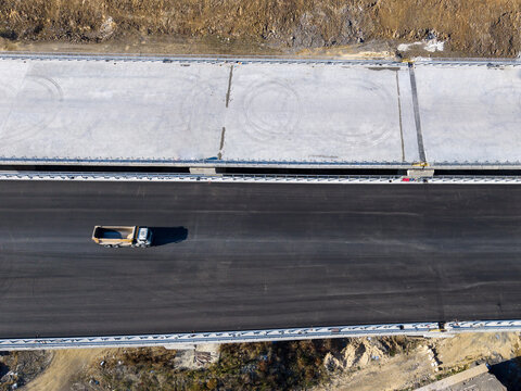Aerial view of a highway construction site featuring a dump truck on fresh asphalt, concrete bridge sections, and earthworks in Istanbul, Istanbul, Turkiye.