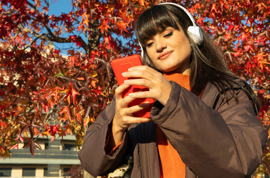 Young woman enjoying music on smartphone in autumn park