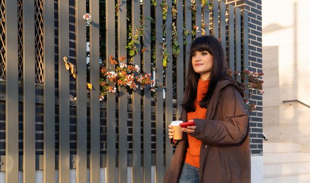 Woman walking in city holding coffee and phone