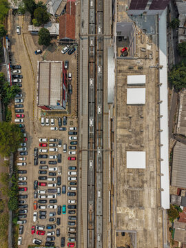 Aerial view of Stasiun Rawa Buntu with commuter trains parked at the platform and a large parking lot filled with numerous cars in Kecamatan Serpong, Banten, Indonesia.