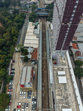 Aerial view of Stasiun Rawa Buntu, showing railway tracks, adjacent apartment building, parking area with cars, and urban infrastructure. Kecamatan Serpong, Banten, Indonesia.