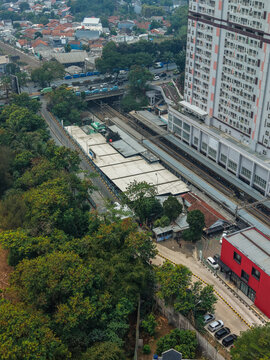 Aerial view of Stasiun Rawa Buntu with railway tracks, station platforms, surrounding urban buildings, and lush trees in Kecamatan Serpong, Banten, Indonesia.