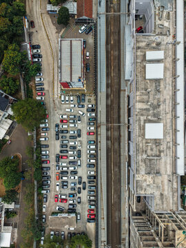 Aerial view of Stasiun Rawa Buntu with railway tracks and a crowded parking lot filled with cars in Kecamatan Serpong, Banten, Indonesia.