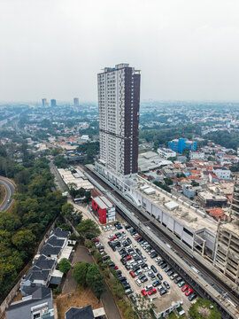 Aerial view of Stasiun Rawa Buntu and a tall apartment building with a busy parking lot, railway tracks, and surrounding urban landscape in Kecamatan Serpong, Banten, Indonesia.