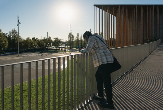 Young man using phone on university campus bridge