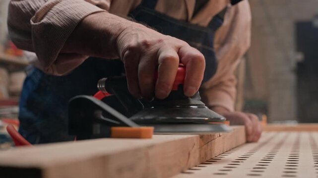 Senior Caucasian carpenter wearing protective respirator sanding wooden timber with orbital sander. Footage suited for occupational safety campaigns, carpentry tutorials and craftsmanship promo
