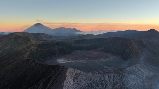 Drone panorama of Mount Bromo volcanic crater at sunset with pastel sky and misty mountain ridges.