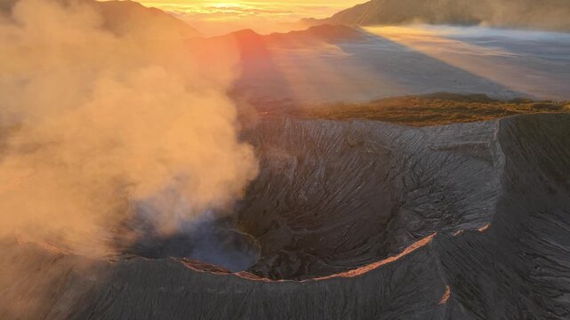 Golden light dances over smoking crater. Misty haze rises from volcanic Bromo Crater