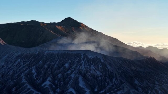 Aerial view of Mount Bromo at sunset with steaming crater and textured volcanic ridges.