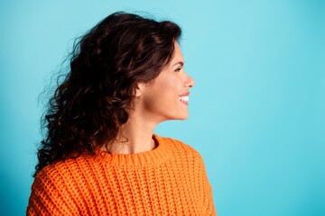 Smiling woman in orange sweater looking to the side against a bright blue background, casual profile portrait conveying happiness, confidence and a relaxed upbeat mood © deagreez