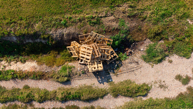 Aerial view of a pile of discarded wooden pallets resting on a dirt path in a grassy field in Milan, Lombardy, Italy.