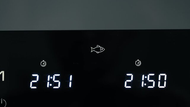 Close-up of air fryer digital display showing fish icon and dual timer settings, kitchen appliance footage. High quality 4k footage