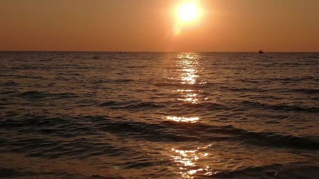 video of a serene ocean during the golden hour sunset. The warm, casting sparkling golden reflections across the gentle waves, with the faint silhouette of a ship sailing in the distance