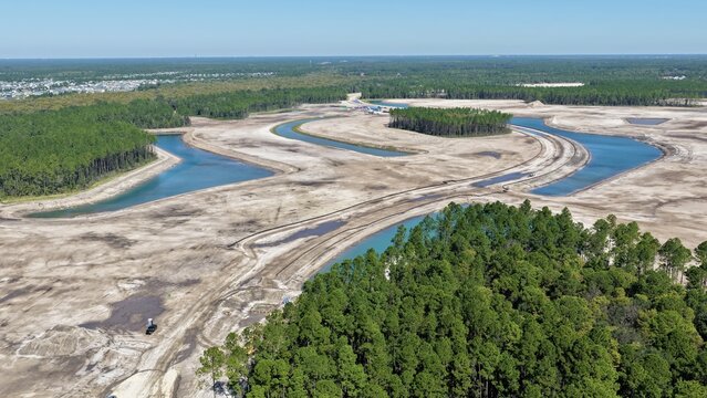 Aerial view of a land development site featuring winding water channels, cleared sandy ground, and surrounding pine forests in St. Johns County, Florida, United States.