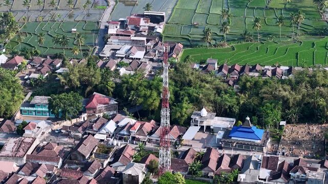 Drone aerial view of Candipuro village with rice terraces, coconut palms, rooftops, and communication tower.