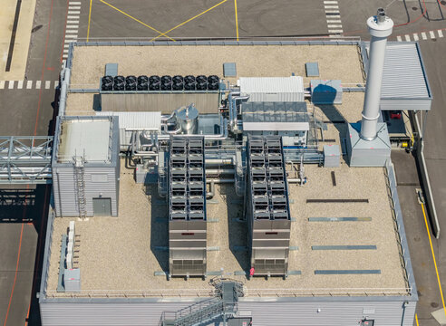 Aerial view of a factory rooftop with industrial cooling units, rows of ventilation fans, mechanical equipment, pipelines and a tall exhaust stack in France.