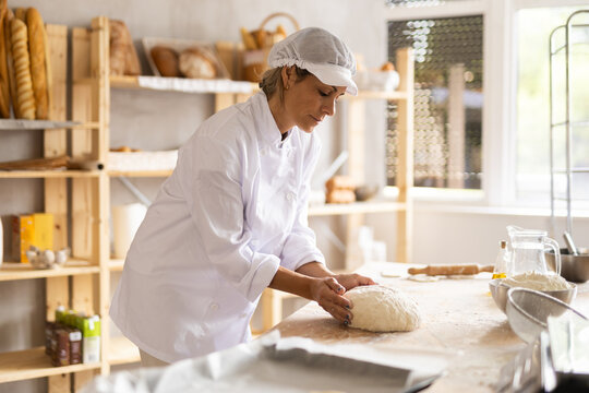 Elderly woman kneads dough in bakery