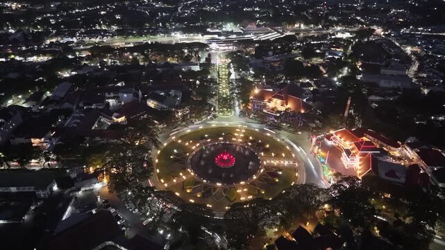 Aerial night view of Alun Alun Malang plaza with illuminated fountain roundabout and surrounding colonial architecture.