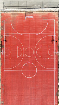 Aerial view of a red multi-purpose sports court with white markings, basketball hoops, and a handball goal in Murla, Valencian Community, Spain.