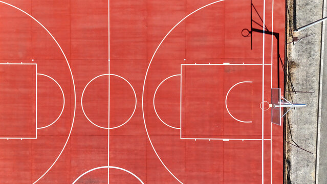 Aerial view of a vibrant red basketball court with white markings and a hoop in Murla, Valencian Community, Spain.